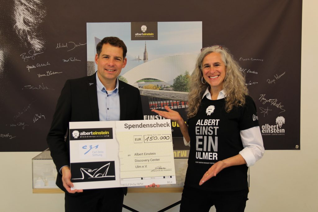 Felix Streiter von Zeiss übergibt den Spendenscheck an Nancy Hecker-Denschlag